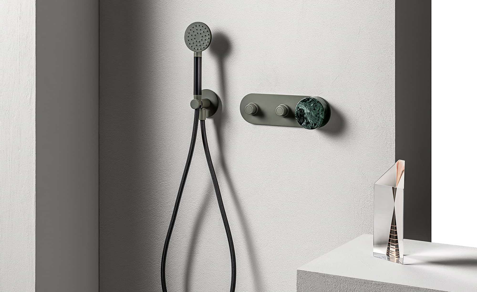 L'immagine rappresenta un sistema doccia incasso di lusso, composto da un doccino con flessibile scuro e una piastra di comando che combina una finitura verde opaco con una manopola in pregiato marmo verde.